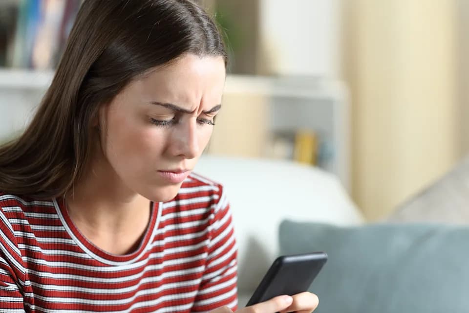 Woman looking suspiciously at an unexpected text message on her smartphone.