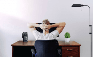 Man sitting at desk with hands clasped behind his head